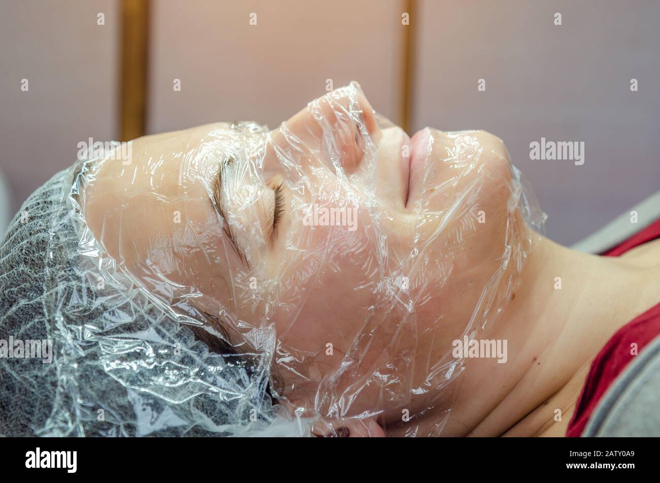 Das Gesicht der Frau ist mit Plastikfolie im Schönheitssalon bedeckt Stockfoto