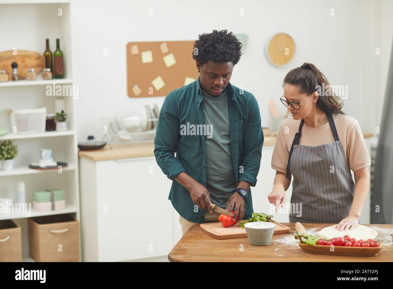 Afrikanischer junger Mann, der mit seiner Frau, die Teig zubereitete, Gemüse auf dem Schneidebrett schneidet, den sie in der Küche zu Hause kochen Stockfoto