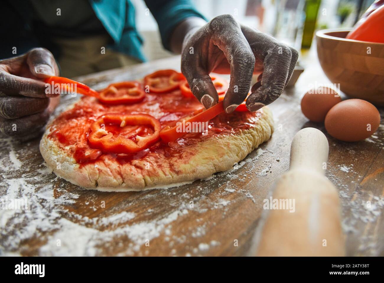 Nahaufnahme des Afrikaners, der Pfeffer auf den Teig legt und zum Abendessen pflanzliche Pizza am Tisch zubereitet Stockfoto