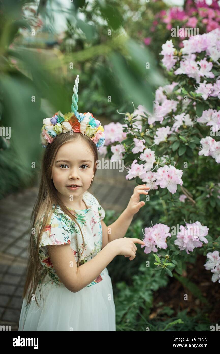 Fantasy-Mädchen mit Regenbogeneinhorn mit Blumen im Azalea-Park. Für Halloween Stockfoto