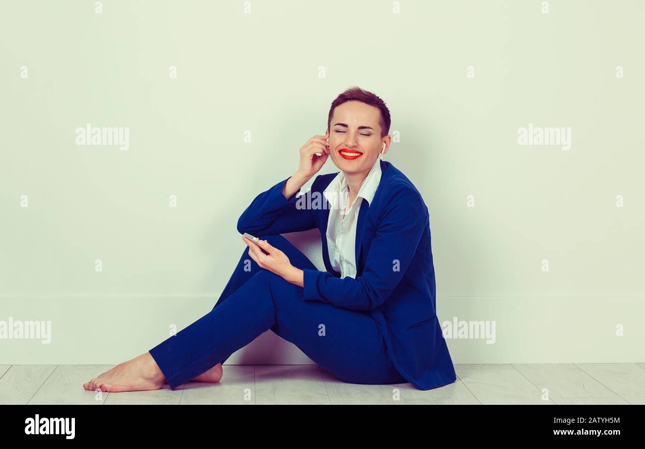 Frau, die Musik hört Sprachnachricht Fröhliches, fröhliches Mädchen begeistert von ihrem Lied hört sie auf dem Handy sitzen auf dem hellen Farbboden Home Corporate Stockfoto