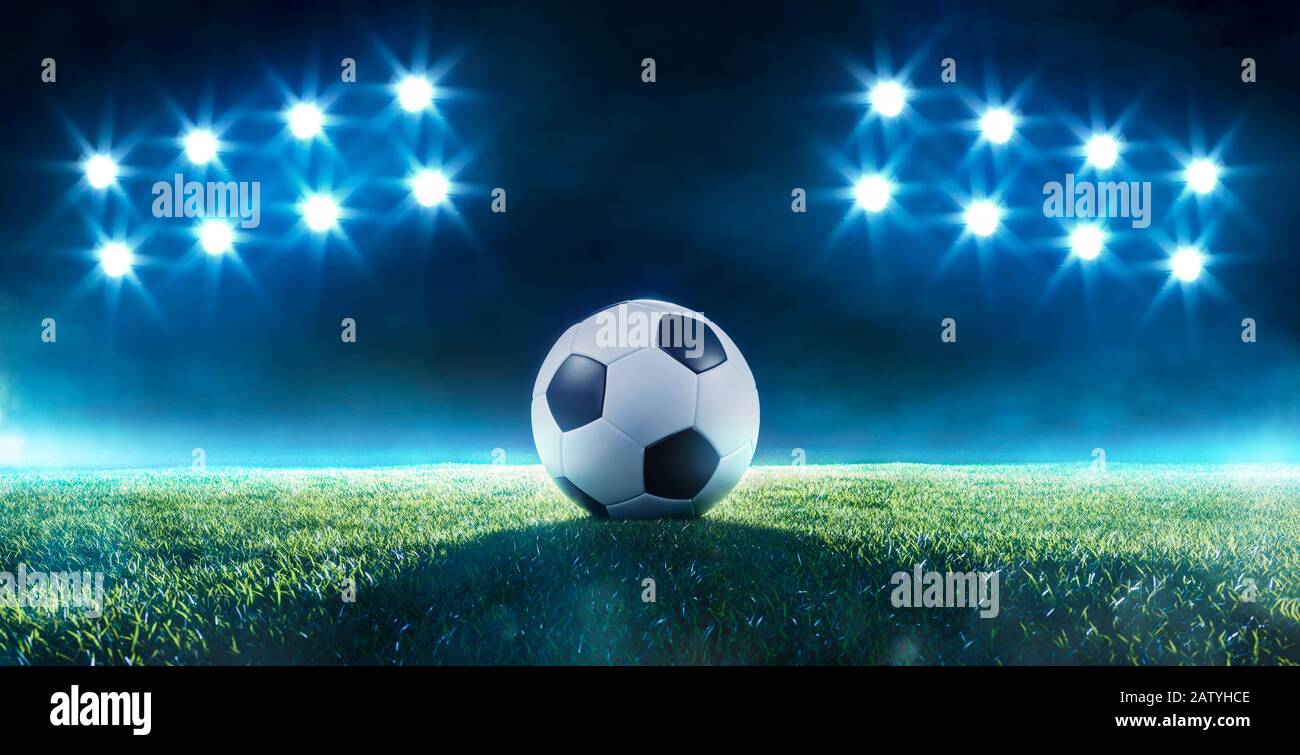 Fußball auf einem Fußballfeld, das von zwei Bänken mit acht leuchtenden Lichtern in einer Rasenansicht mit Nebel beleuchtet wird Stockfoto