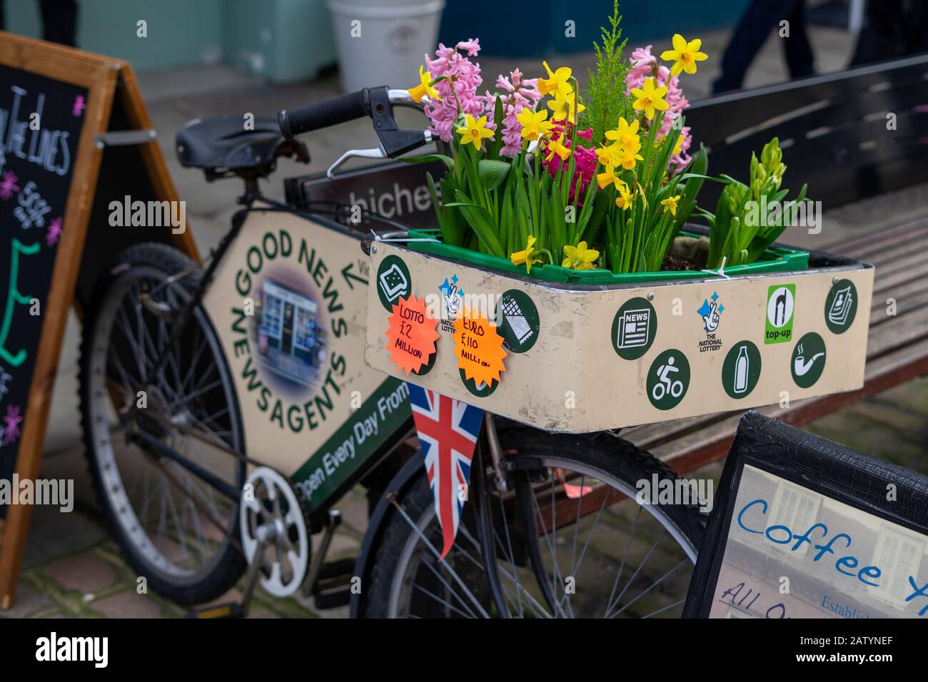 Frühlingsblumen im Korb eines alten Fahrrades vor einem Zeitungskiosk Stockfoto