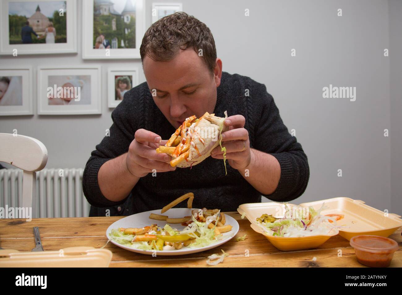 Ein Mann, der zu Hause sitzt und einen Dönner Kebab und Chips zum Mitnehmen mitnimmt, Großbritannien Stockfoto