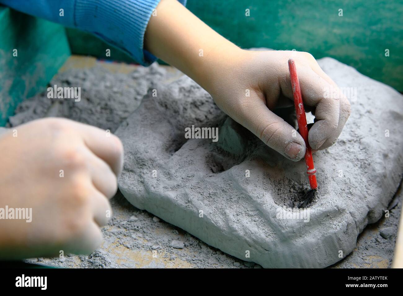 Kind, das Fossil-, Mineral- und Schatzgräbenspiel spielt. Das Kind verwendet Werkzeuge, z. B. eine Bürste. Stockfoto