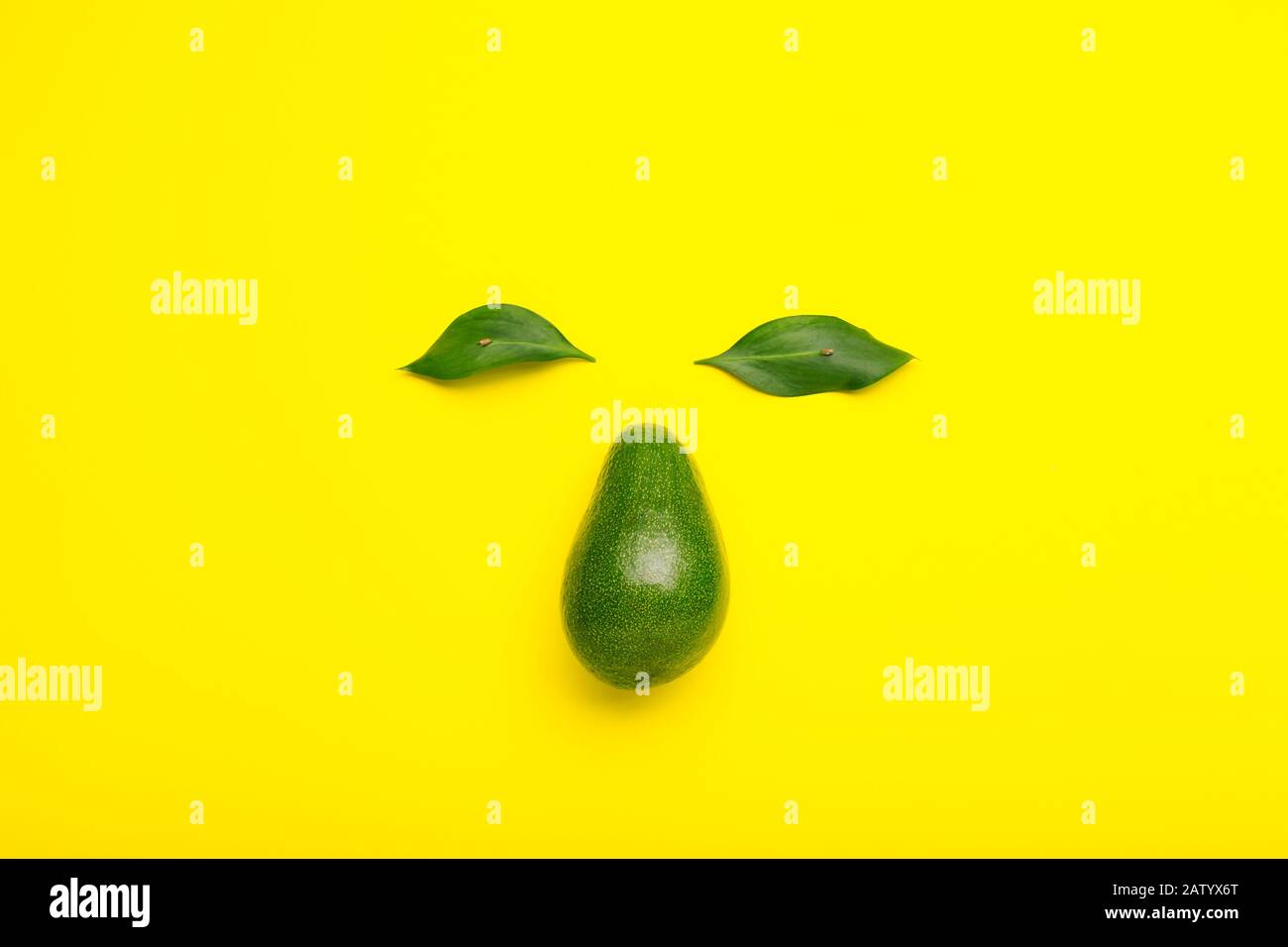 Kreatives Gesicht aus Avocado und grünen Blättern. Minimaler Stil Sommerfrucht flach lag Avocado auf gelbem Farbhintergrund. Stockfoto