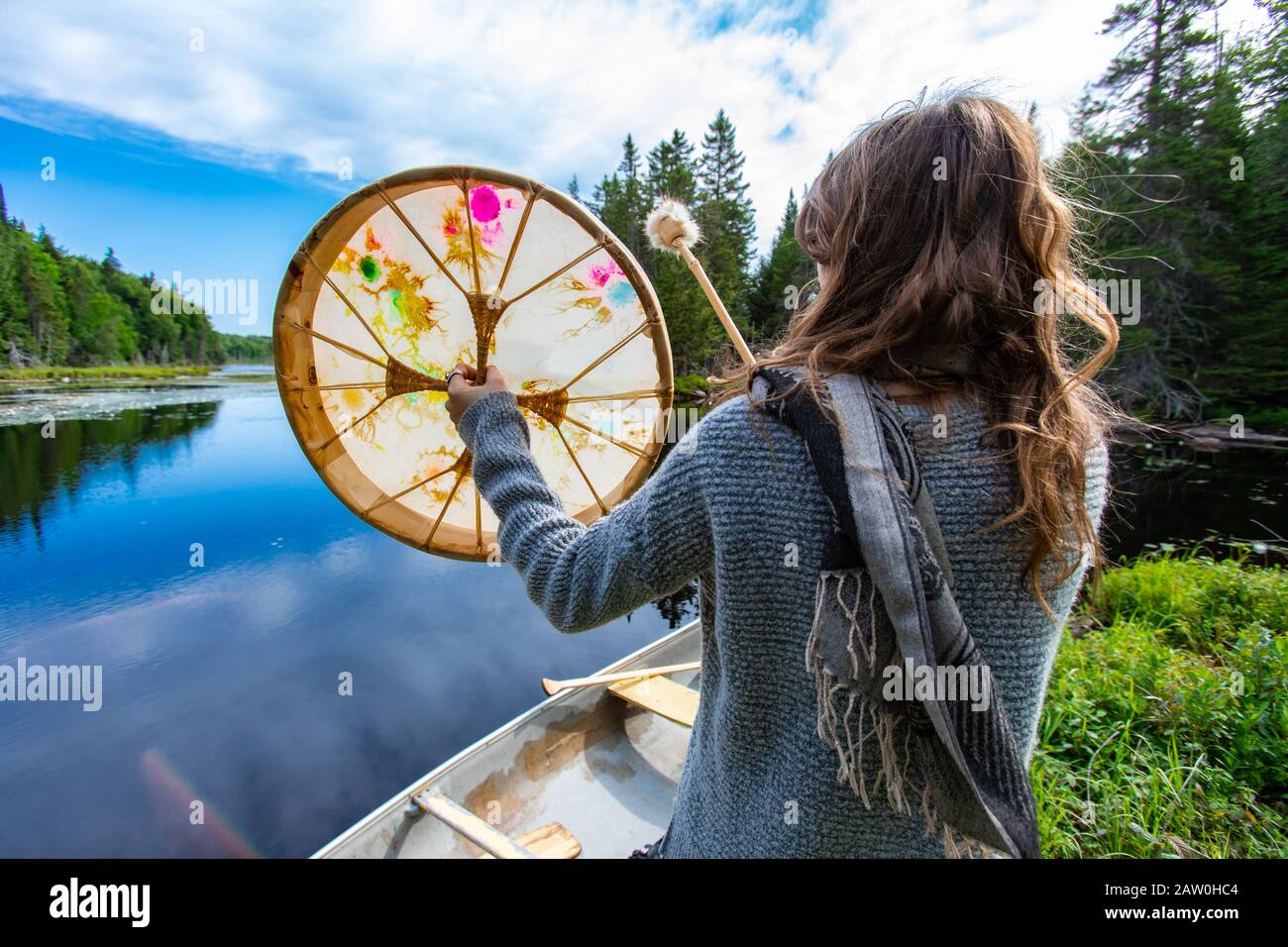 Rückansicht der jungen Frau, die mit einem mit Pelz überzogenen Stock in der Nähe eines Kanus in Richtung See im Norden Quebecs, Kanada, spielt Stockfoto