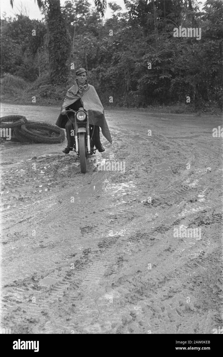 Fotoreportage Palembang niederländischer Soldat auf einem Motorrad, eingewickelt in regencap, auf einer schlammigen Straße unterwegs. In der Ecke sind Rollen mit Stacheldraht Datum: Januar 1947 Ort: Indonesien, Niederländische Ostindien, Palembang, Sumatra Stockfoto