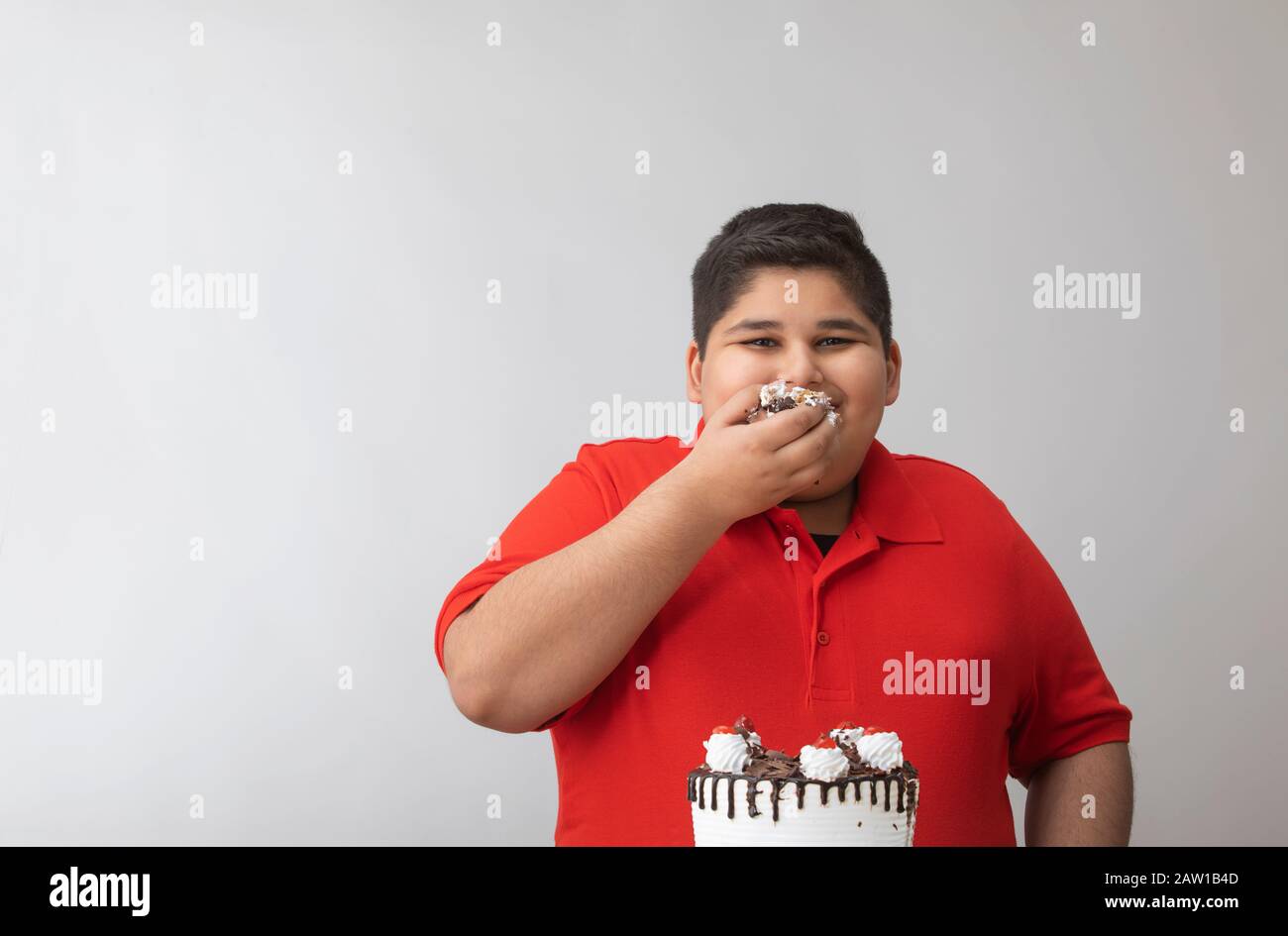 Kleiner Junge verschlingt den Kuchen mit den Händen. (Fettleibigkeit) Stockfoto