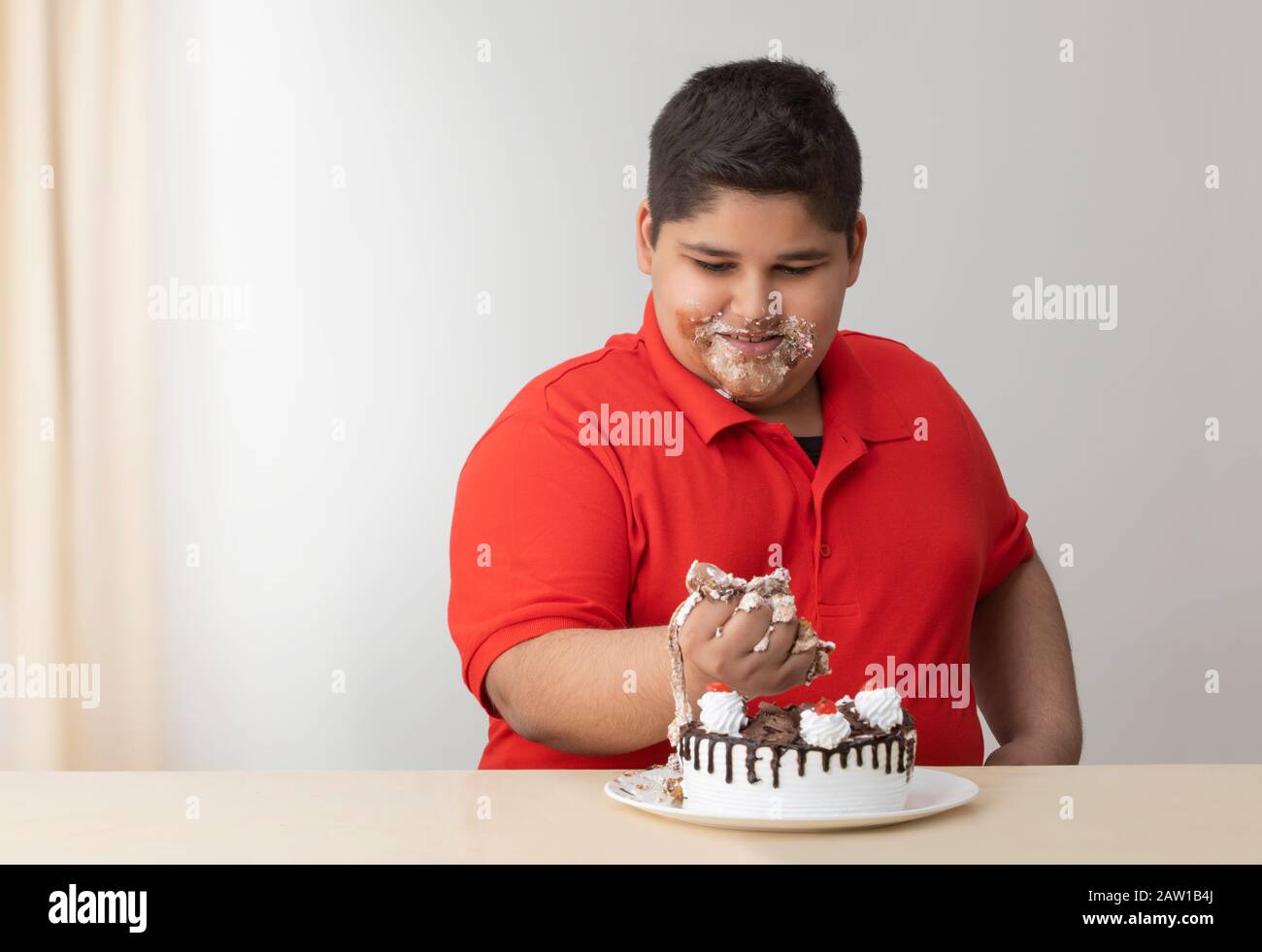 Kleiner Junge, der seinen Mund mit Kuchen betäubt. (Fettleibigkeit) Stockfoto