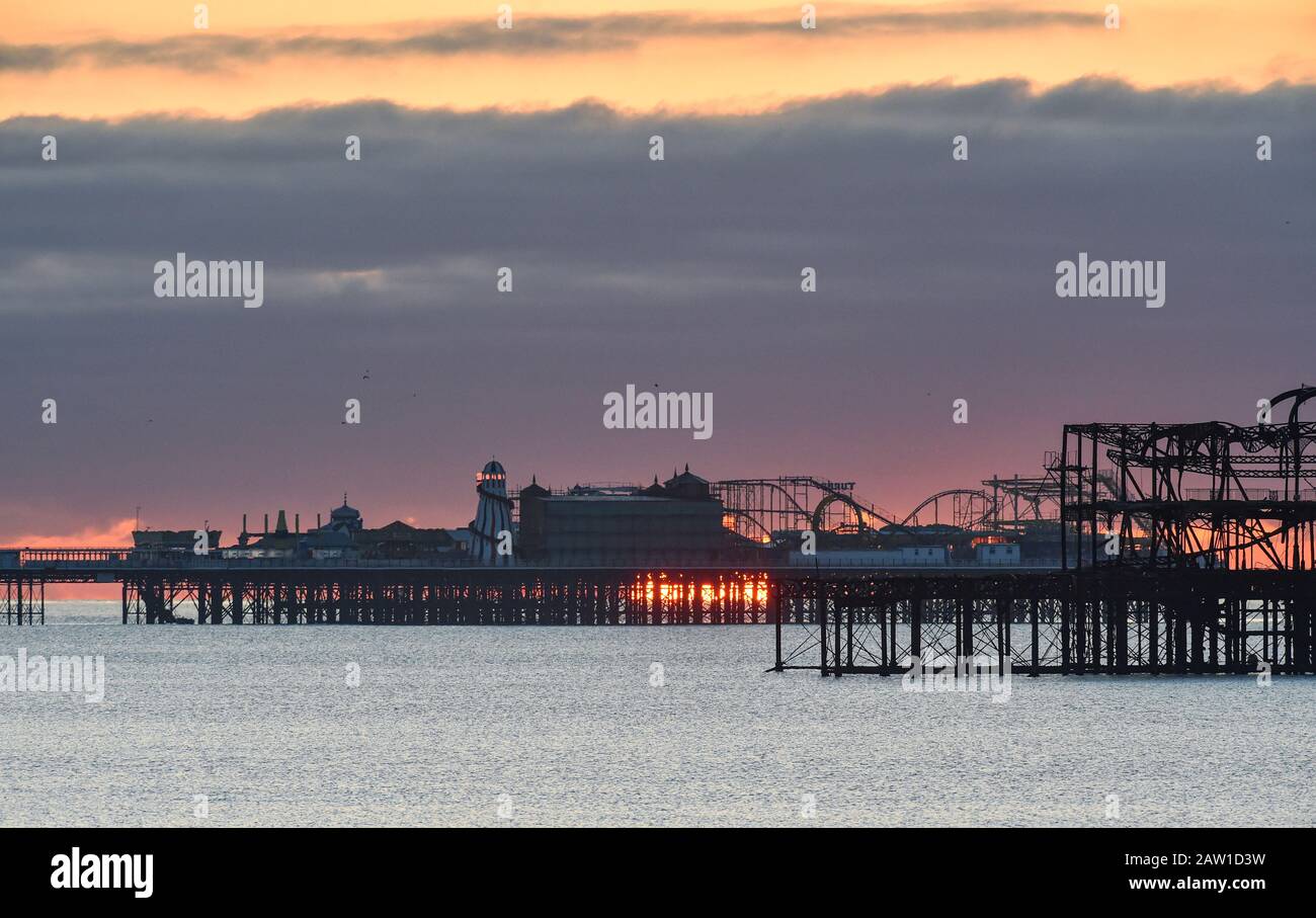 Brighton UK 6. Februar 2020 - Die Sonne steigt hinter Brightons zwei Piers an einem kalten hellen Morgen auf. Für die nächsten paar Tage wird in Großbritannien ein noch feineres Wetter prognostiziert, bevor das stürmische Wetter am Wochenende eintreffen wird. Kredit: Simon Dack / Alamy Live News Stockfoto