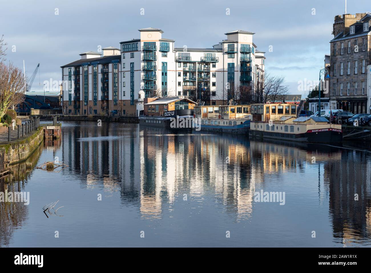 Modernes Apartmentgebäude am Flussufer und Wassergräte am Ufer spiegelten sich im Wasser von Leith in Leith, Edinburgh, Schottland, Großbritannien, wider Stockfoto