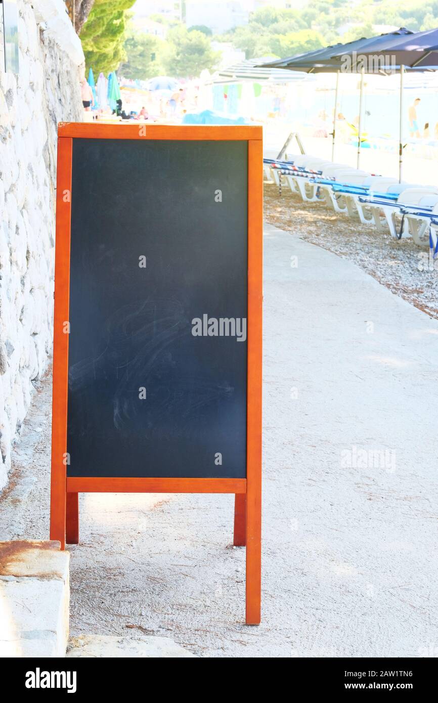 Schwarzes Board-Menü schwarze Farbe für Text, Nachricht oder Werbung. Mockup steht in der Nähe des Cafés an der Küste. Sonniger Tag. Stockfoto