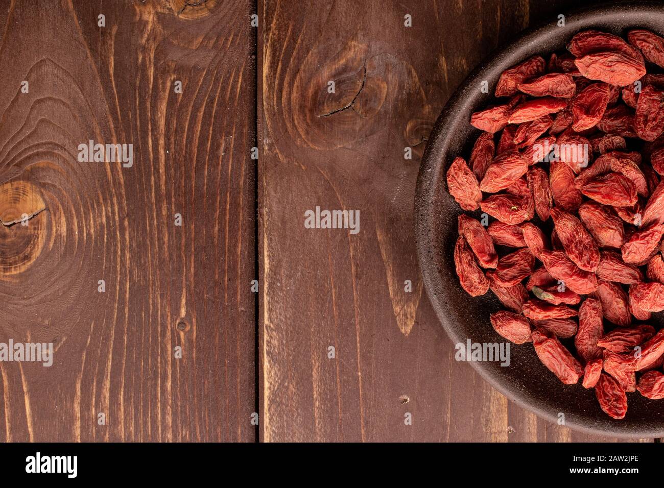 Viel getrockneter roter Goji mit brauner Keramikachterbahn auf braunem Holz Stockfoto