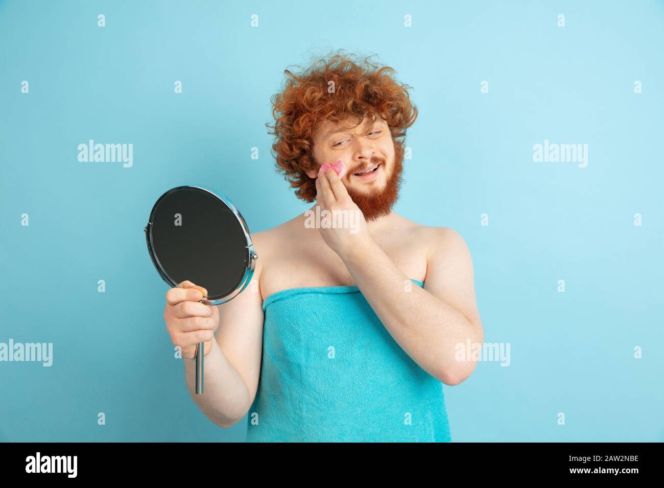 Porträt des jungen kaukasischen Mannes in seinem Schönheitstag und Hautpflege Routine. Männliches Modell mit natürlichem rotem Haar, das Feuchtigkeitscreme aufgibt, Öle auf Fakeskin. Körper- und Gesichtspflege, natürliches, männliches Schönheitskonzept. Stockfoto