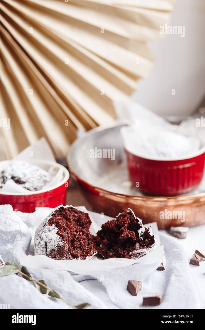 Schokoladenmuffins in roten Tassen. Kleines glasiertes Keramikramekin mit braunen Kuchen auf grauem und weißem Grund Stockfoto