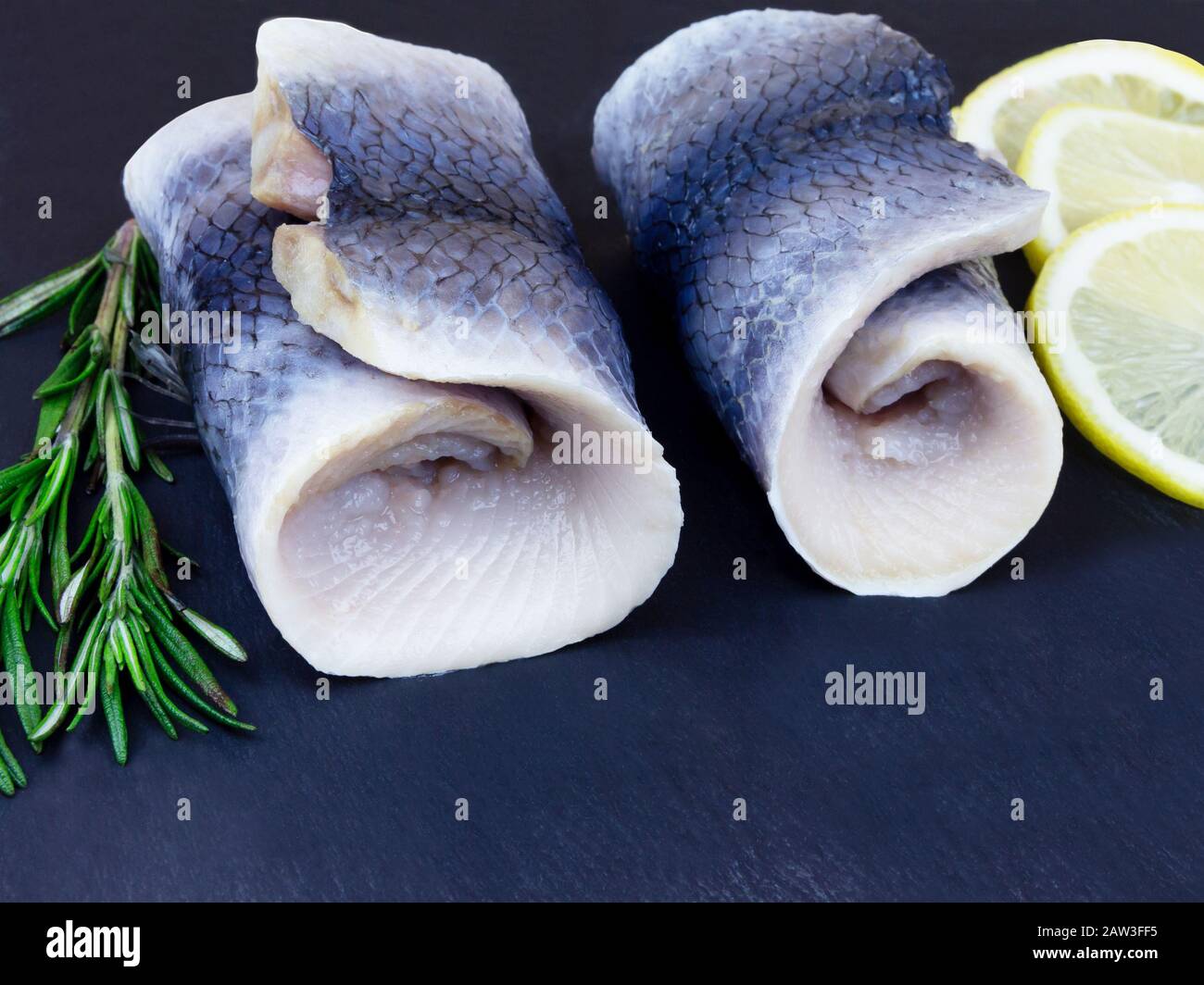 Heringsrollen mit Schnittlauch und Zitronenbeilchen auf dunklem Hintergrund Stockfoto