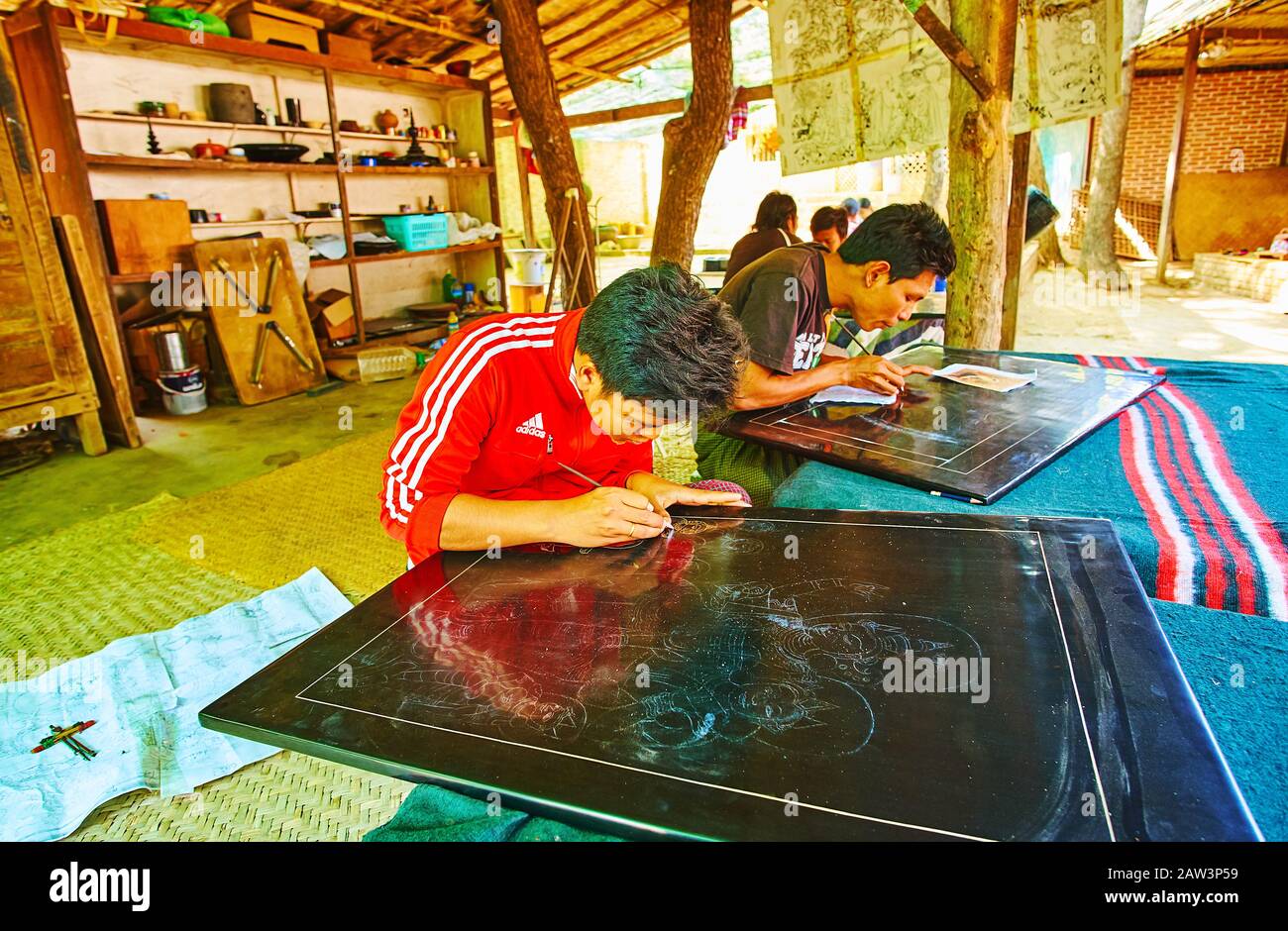 Bagan, MYANMAR - 25. FEBRUAR 2018: Der junge Kunsthandwerker macht die Bilder auf Lackplatten, indem er Radnadeln und andere Werkzeuge in traditionellen Baumaschinen verwendet Stockfoto