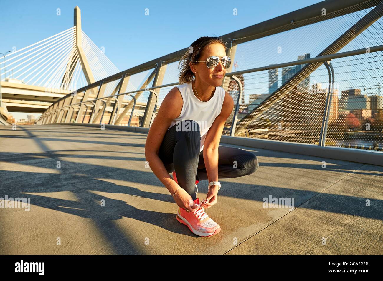 Eine athletische Frau bindet ihren Schuh vor der Zakim Bridge in Boston Stockfoto