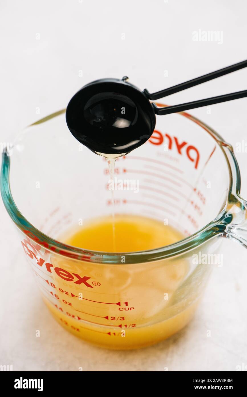 Messlöffel wird verwendet, um Öl zu einem Pyrex Messbecher Rezept hinzuzufügen Stockfoto