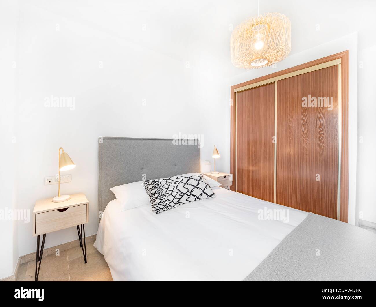 Komfortables Hotelzimmer mit Filzkopfteil mit Naturstoffkissen, Rattan-Lampe, Nachttisch aus Holz und einem großen Holzkissen. Urlaubsziel a Stockfoto
