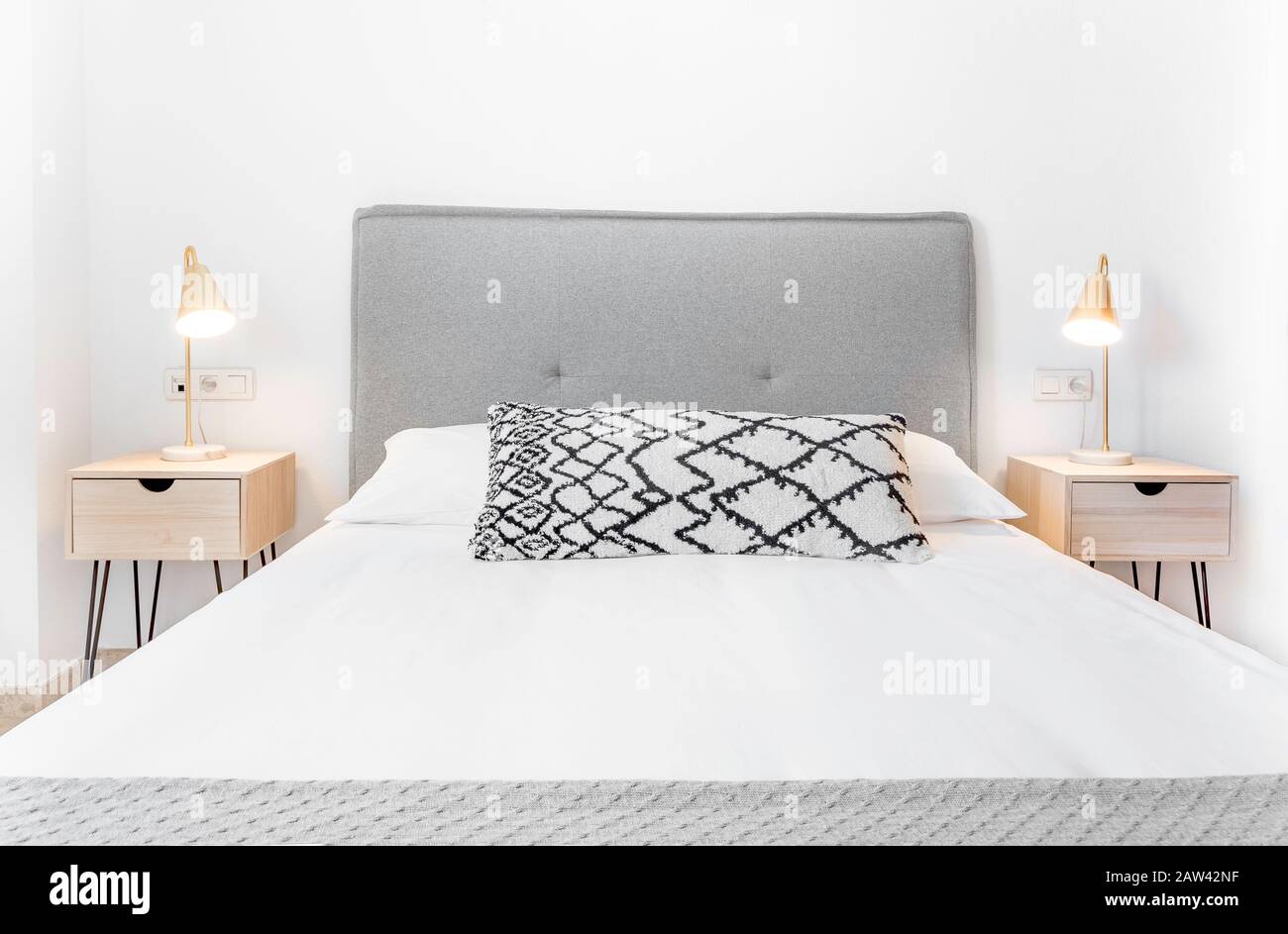 Komfortables Hotelzimmer mit Filzkopfteil mit Naturstoffkissen, Metalllampen, Nachttisch aus Holz und einem großen Kissen.Holiday Destination Apartment Stockfoto