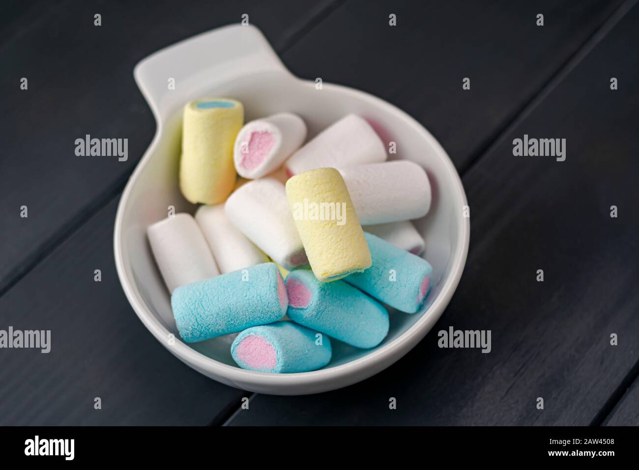 Eine weiße Schüssel mit Süßigkeiten verschiedener Farben, die von Kindern auf einer Party über einem grauen Holztisch verzehrt werden können Stockfoto
