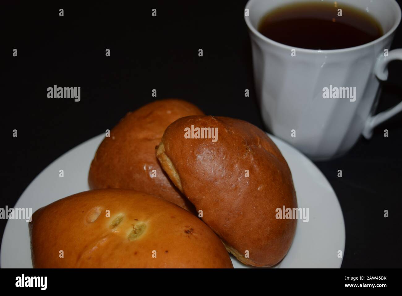 Drei Pasteten auf einem weißen Teller und eine Tasse Kaffee auf schwarzem Hintergrund. Nahaufnahme Stockfoto