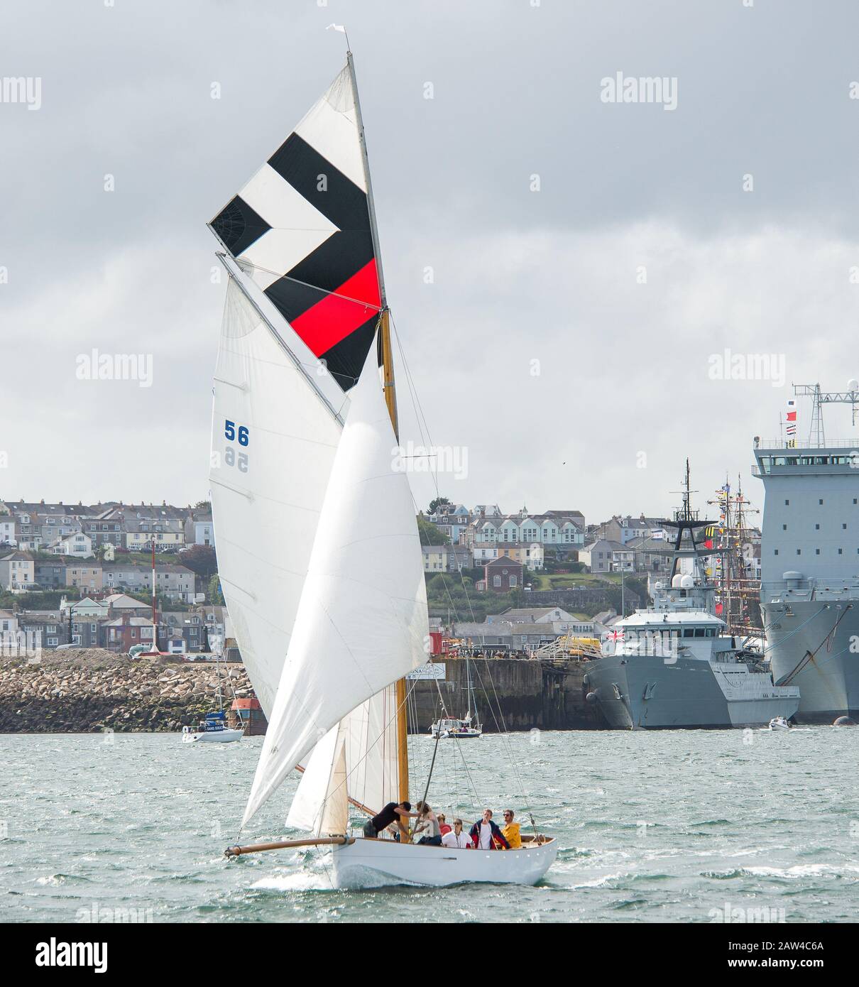 Traditionelles Falmouth Arbeitsboot mit voller Segeltörn in der Brise der Fal-Flussmündung, das gegen das moderne graue Marineschiff und die Skyline von Falmouth rast Stockfoto