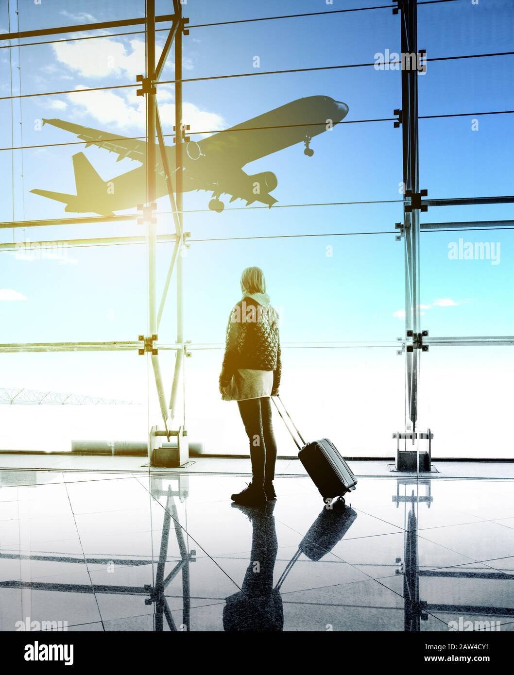 Frau, die vom großen Fenster auf den Flughafen blickt. Sie machen sich Freude an Flugzeugen, die sich auf der Landebahn bewegen Stockfoto