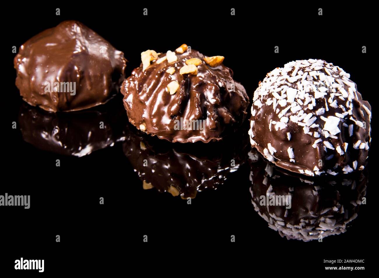 Drei Schokoladenkuchen auf einer schwarzen Spiegeloberfläche mit Kokosspinzen und Haselnuss auf dunklem Grund bestreut Stockfoto