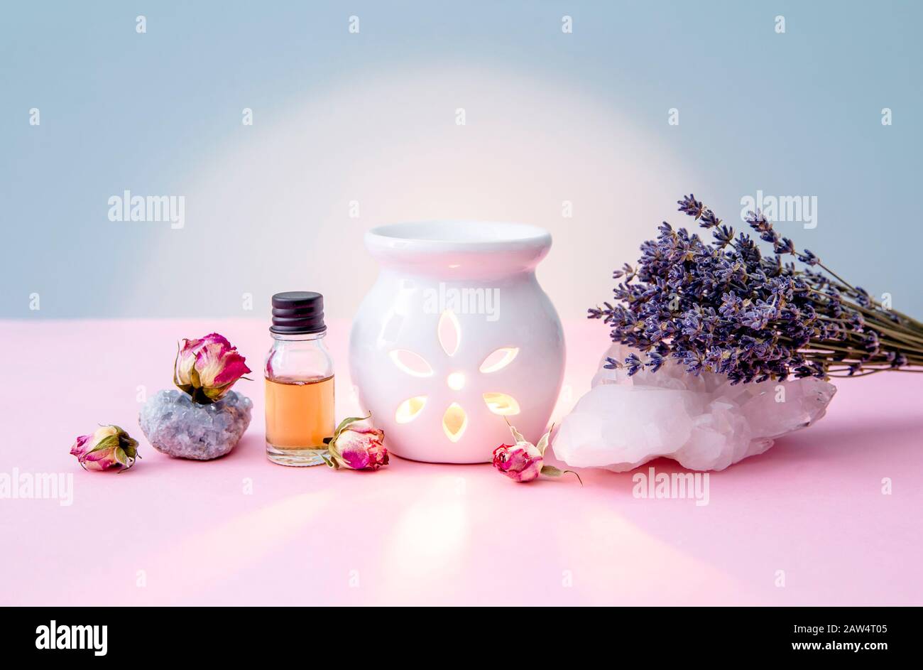Weiße Kerze Aroma Öllampe mit ätherischem Ölbehälter und getrockneten Blumen, Kristallgeoden auf modernem pastellrosa und blauem Hintergrund im Innenbereich. Stockfoto