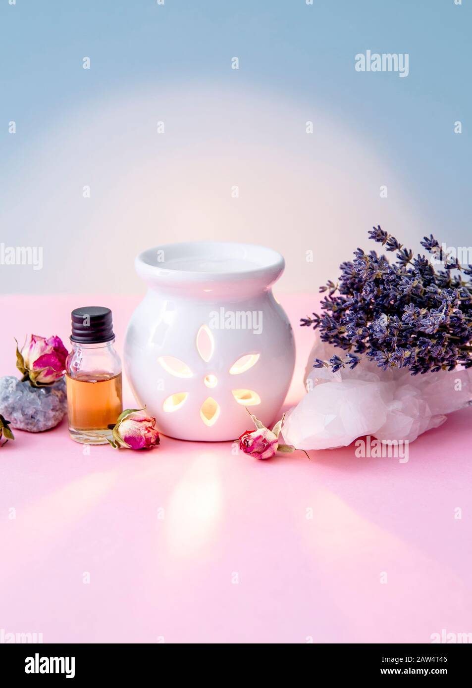 Weiße Kerze Aroma Öllampe mit ätherischem Ölbehälter und getrockneten Blumen, Kristallgeoden auf modernem pastellrosa und blauem Hintergrund im Innenbereich. Stockfoto
