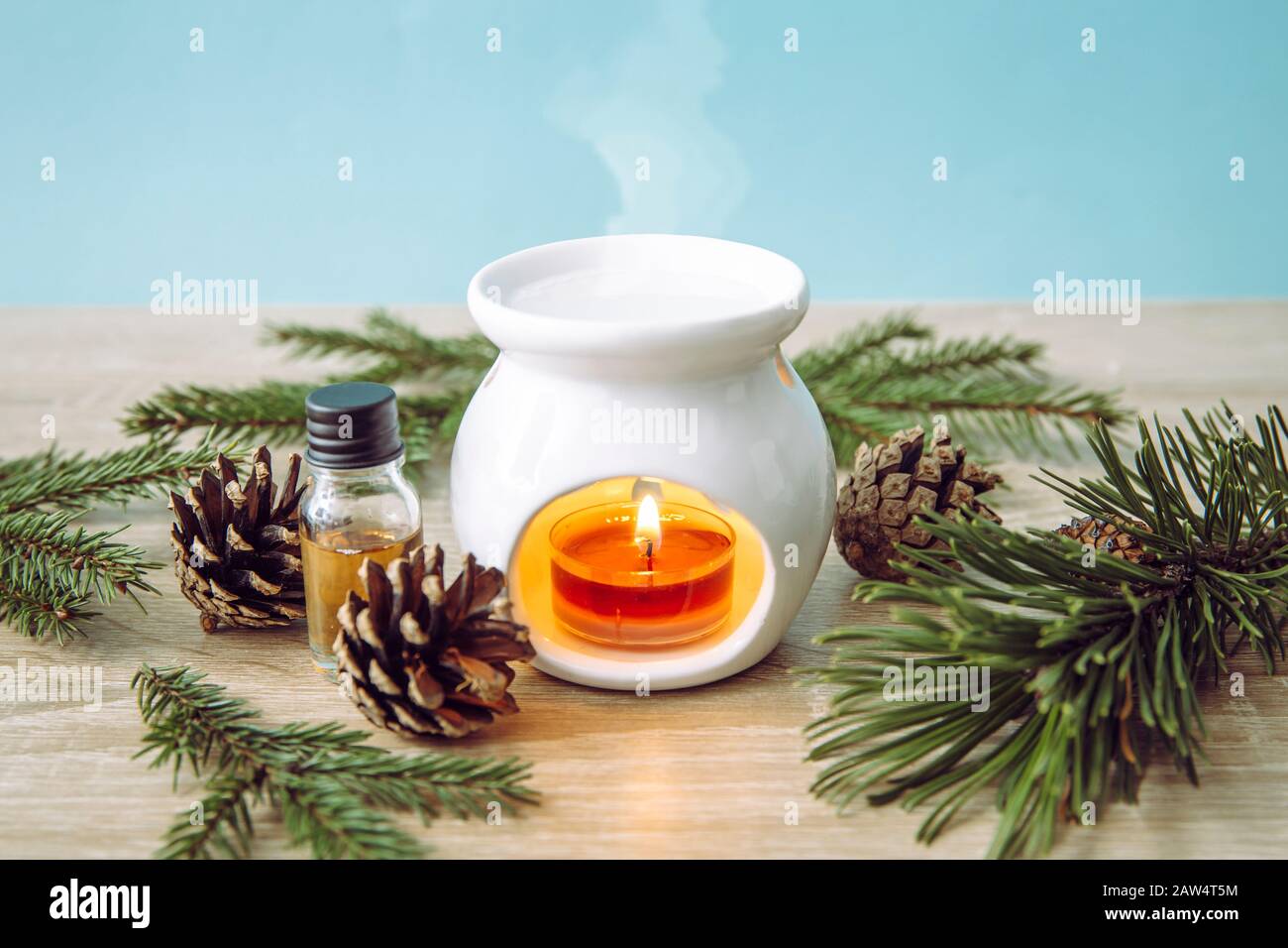 Weiße Kerze Aroma Öllampe mit Kiefernfichte ätherische Ölflasche und Baumzweige zur Dekoration auf Holz- und blauem Grund. Stockfoto