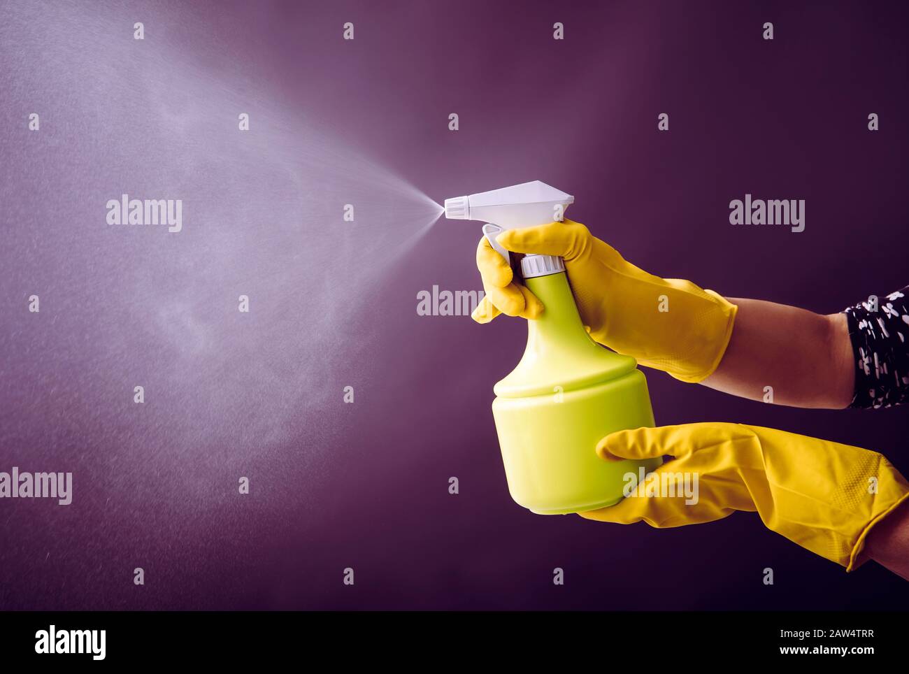 Frau, die gelbe Gummihandschuhe mit grüner Sprühflasche trägt und Flüssignebel in die Luft sprüht, kühler Lichteffekt. Viel Kopierspeicher. Stockfoto