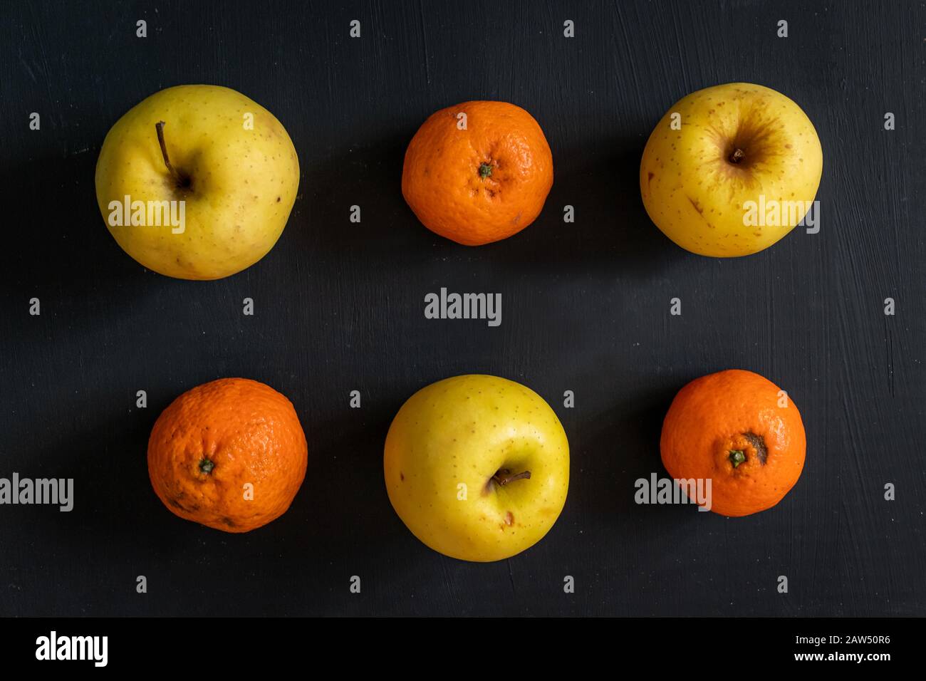 Gelbe Äpfel und Orangen in Reihen über dunklem Hintergrund Stockfoto