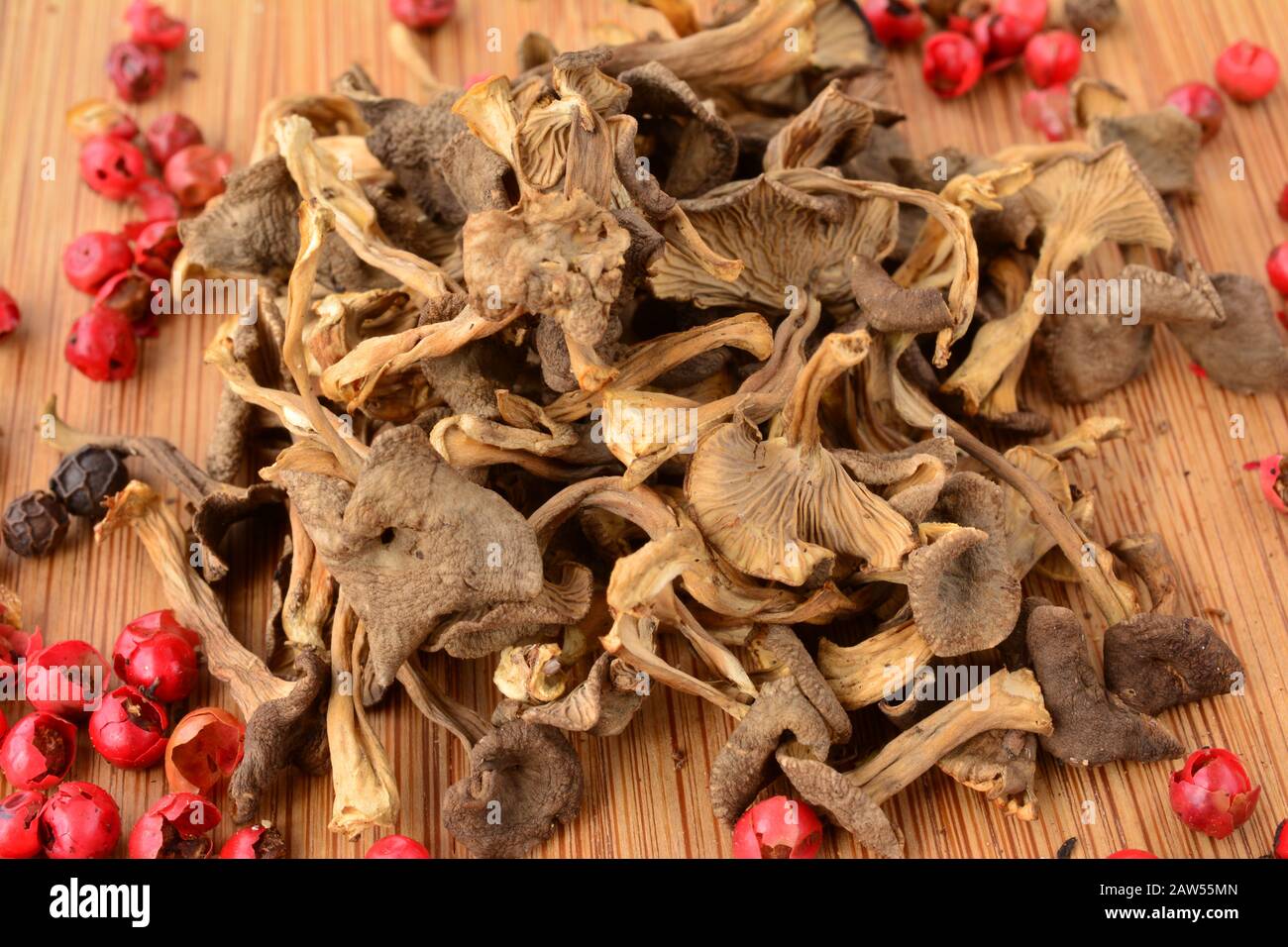 Getrocknete Trumpet Chanterelle oder Cantharellus tubaeformis bereit für die Küche, zusammen mit rotem und schwarzem Pfeffer auf Holzhackbrett, Nahwetteifer Stockfoto