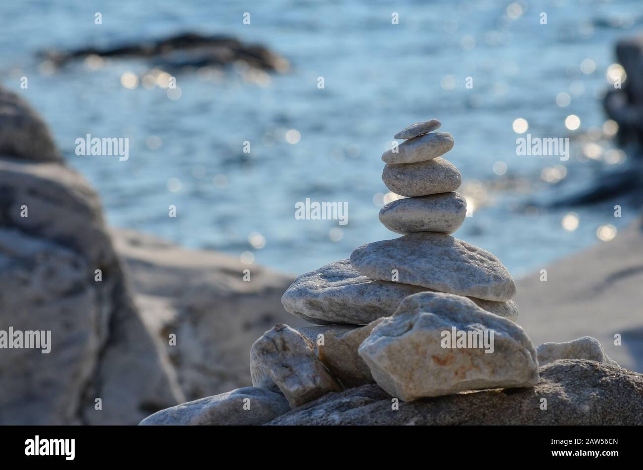 Zen-Steine am felsigen Strand vor Sonnenuntergang vor blauem Bokeh-Hintergrund Stockfoto