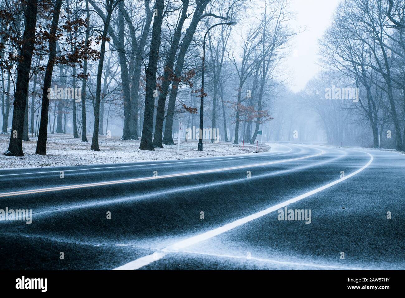 Die Straße ist von Bäumen umgeben, wenn der Schnee am schneebedeckten Wintertag fällt. Stockfoto