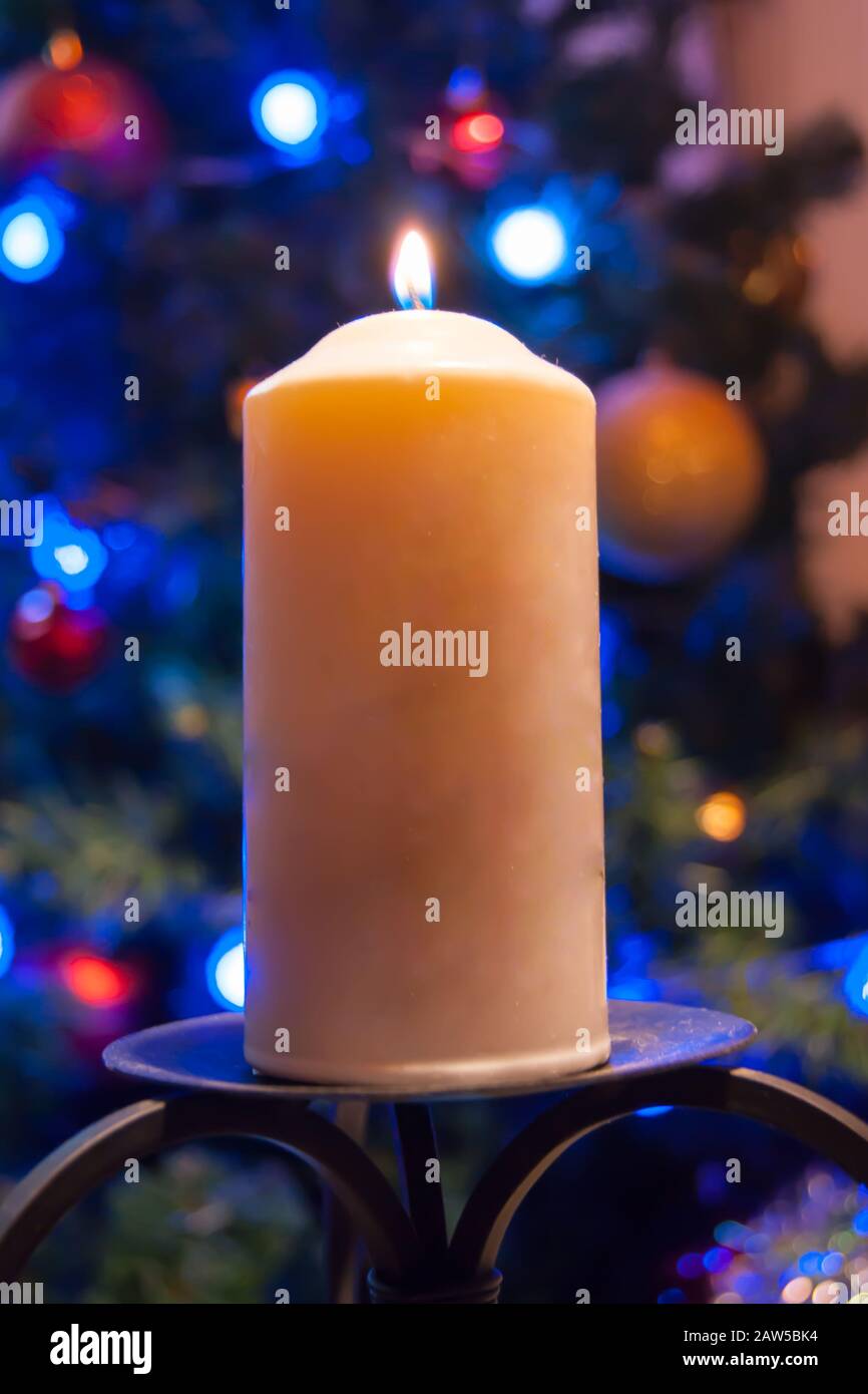 Eine große Kerze brennt vor dem Hintergrund einer Girlande mit strahlendem Licht. Vertikales Foto, Unschärfe. Mystische esoterische Romantik Divination Stimmung getauft Weihnachts-Karol-Setcer Stockfoto
