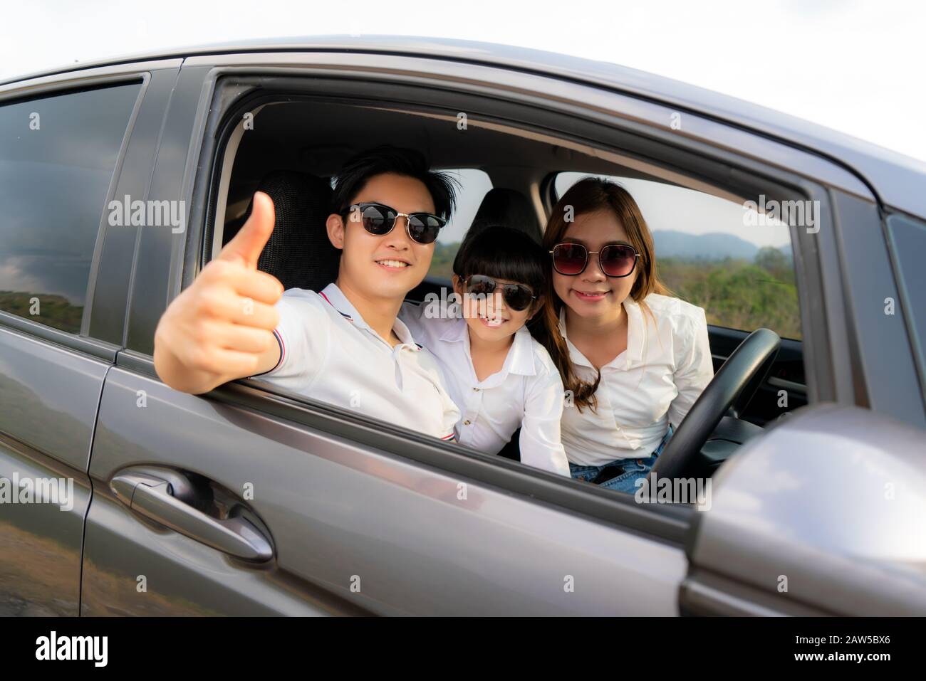 Die glückliche asiatische Familie mit dem Daumen nach oben und Mutter und Tochter tragen Sonnenschutzmittel im Kompaktwagen und lächeln und fahren auf Reisen im Urlaub. KFZ-Versicherung Stockfoto