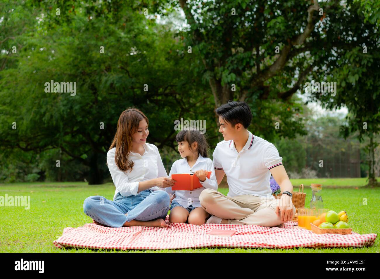 Asiatische Teenager Familie fröhlicher Urlaub Picknick-Moment im Park mit Vater, Mutter und Tochter Lesen Buch und Lächeln zu verbringen Urlaub glücklich zusammen Stockfoto