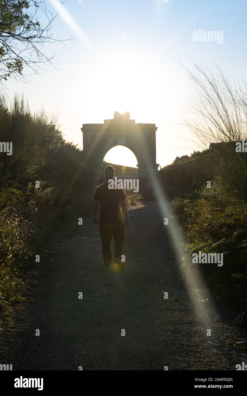 Rückansicht eines Mannes, der auf einer alten Straße mit Sonnenstrahlen bei Sonnenuntergang spazieren geht Stockfoto