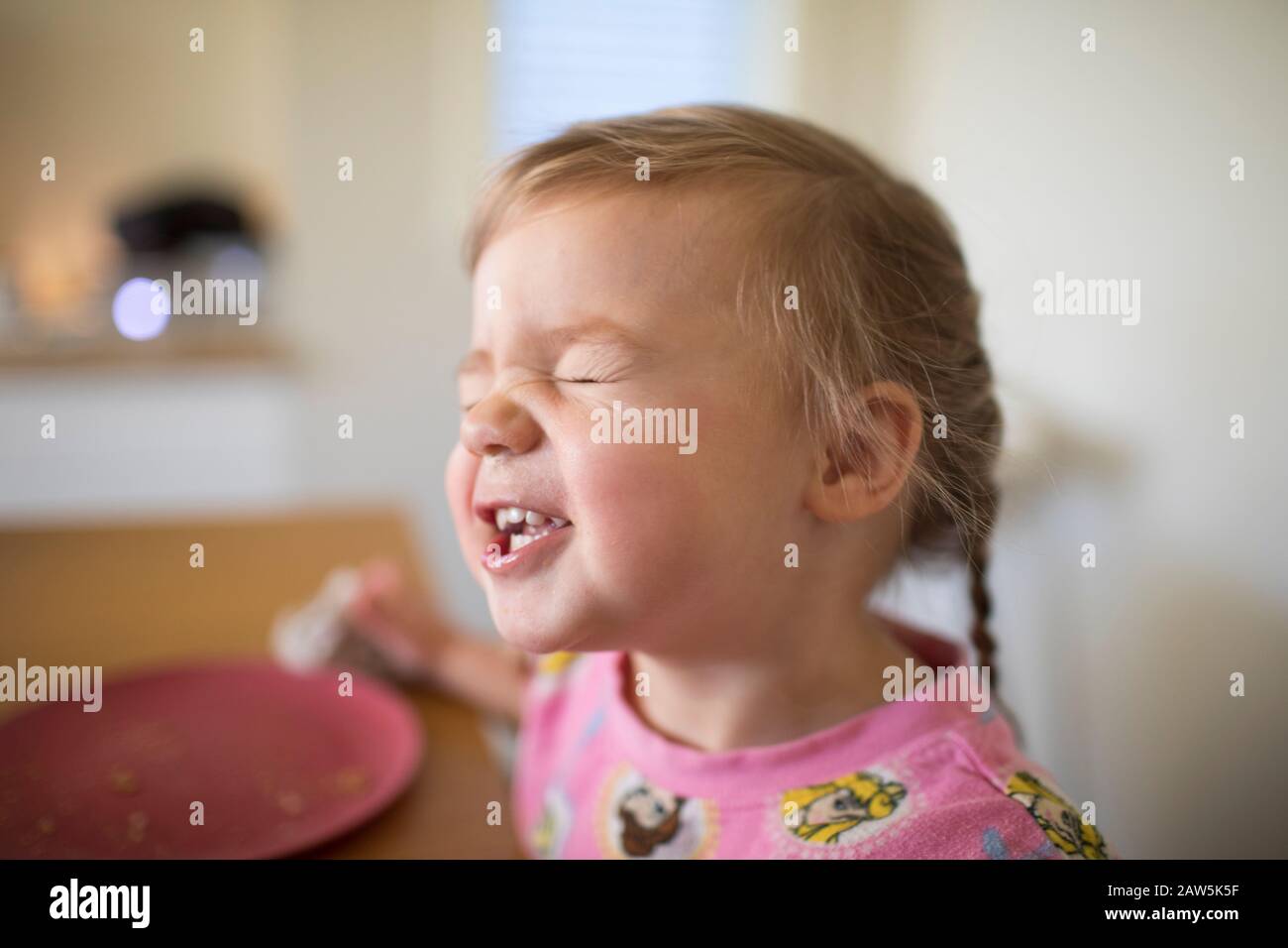 Nettes Kleinkind Mädchen machen lustige Gesichter am Tisch. Stockfoto