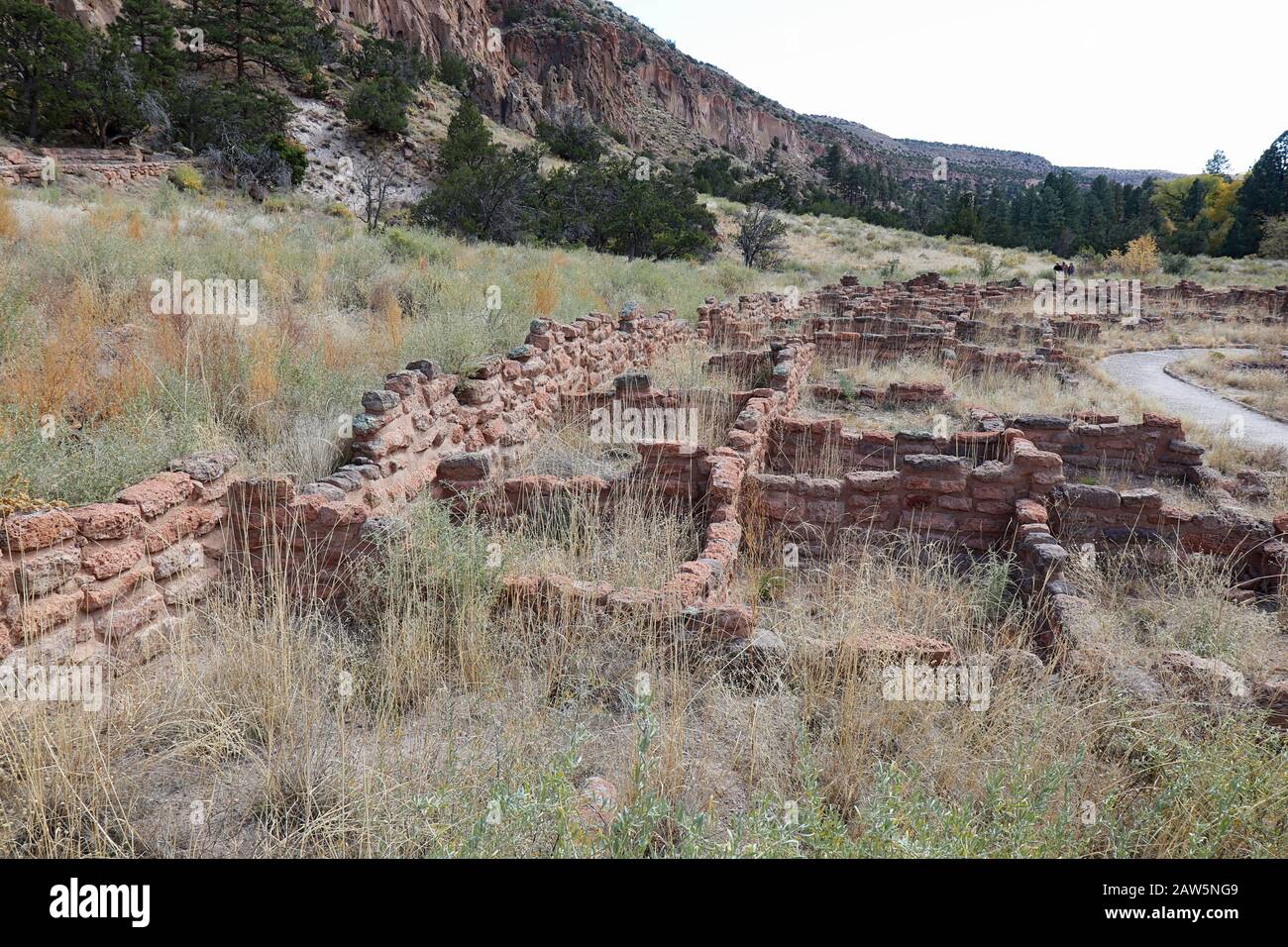 Teil der Tyuonyi-Ruinen der angestammten Pueblo-Völker und unidentifizierbare Wanderer an den Klippen entlang des Hauptschleifenweges im Frijoles Canyon at Band Stockfoto