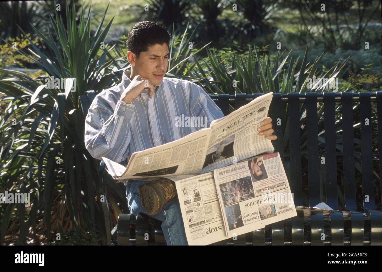 Der 18-jährige hispanische Mann liest spanischsprachige Zeitung, während er auf einer Bank im öffentlichen Park in Austin, Texas sitzt. Stockfoto Der 18-jährige hispanische Mann liest spanischsprachige Zeitung, während er auf einer Bank im öffentlichen Park in Austin, Texas sitzt. Stockfoto