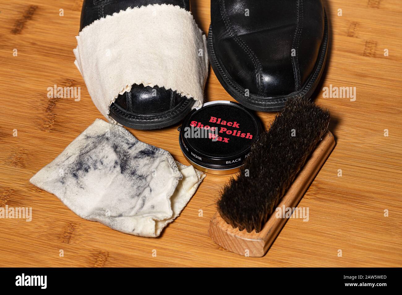 Ein Paar polierfertige Schuhe, umgeben von den für den Prozess verwendeten Zubehörteilen auf einem Holzboden. An verschiedenen Stellen ist Platz für Kopien Stockfoto