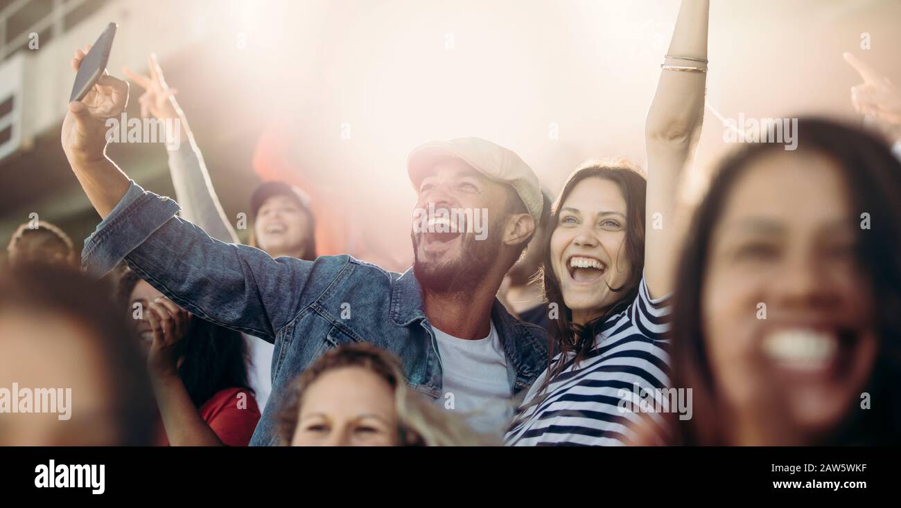 Aufgeregtes Paar jubelt und nimmt selfie im Stadion mit. Fröhliche Fußballfans nehmen selfie beim Spiel im Stadion mit. Stockfoto