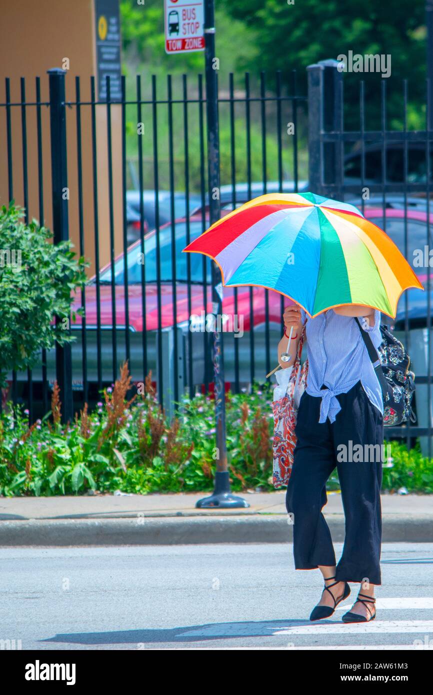 Eine junge Dame schützt sich mit einem bunten Regenbogenschirm vor den Sonnen, die sie in Chicagos Chinatown auf der Straße überquert Stockfoto