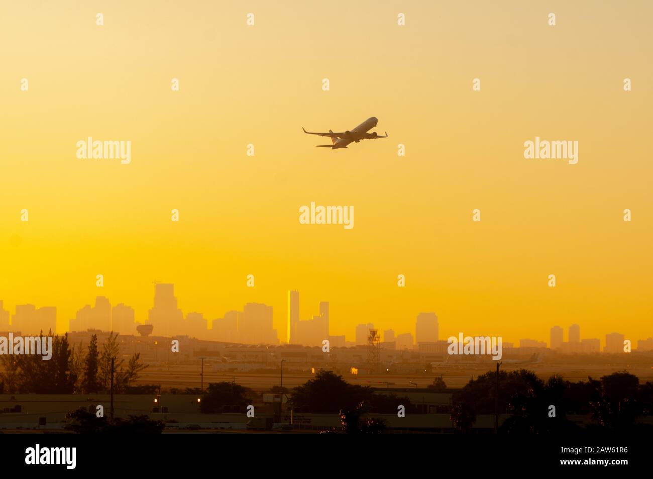 Beim Start vom Flughafen Miami mit der Stadt im Hintergrund wird ein Flugzeug vor einem farbenfrohen Sonnenaufgang in Gelb und Orange silhouettiert. Stockfoto